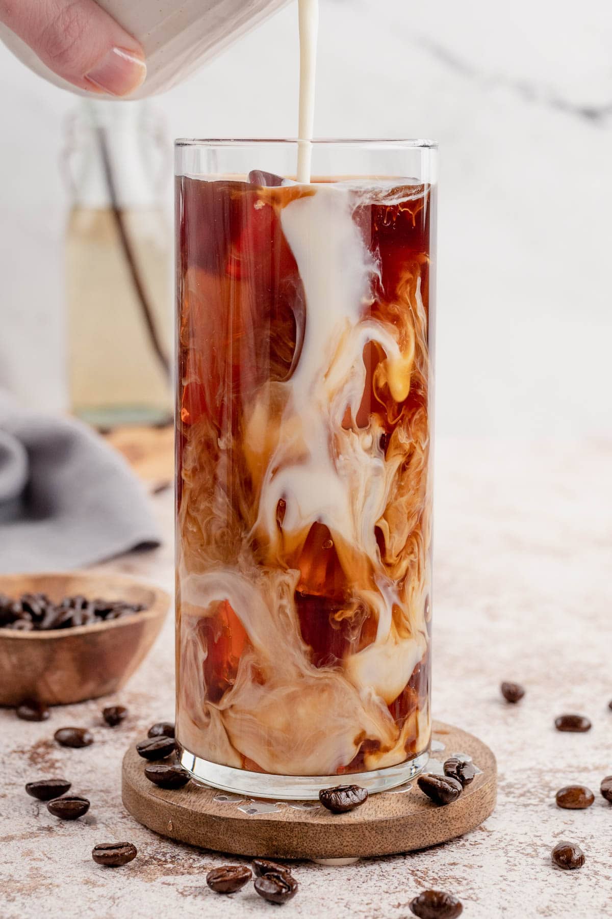 Milk being poured into a glass with beautiful swirls of coffee and cream over iced cubes.