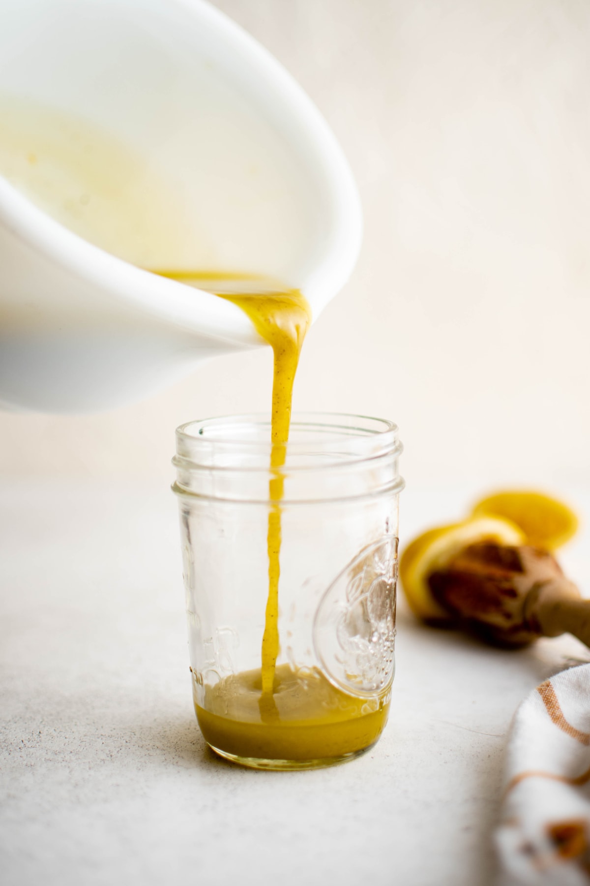 Pouring a vinaigrette from a white bowl into a glass jar.