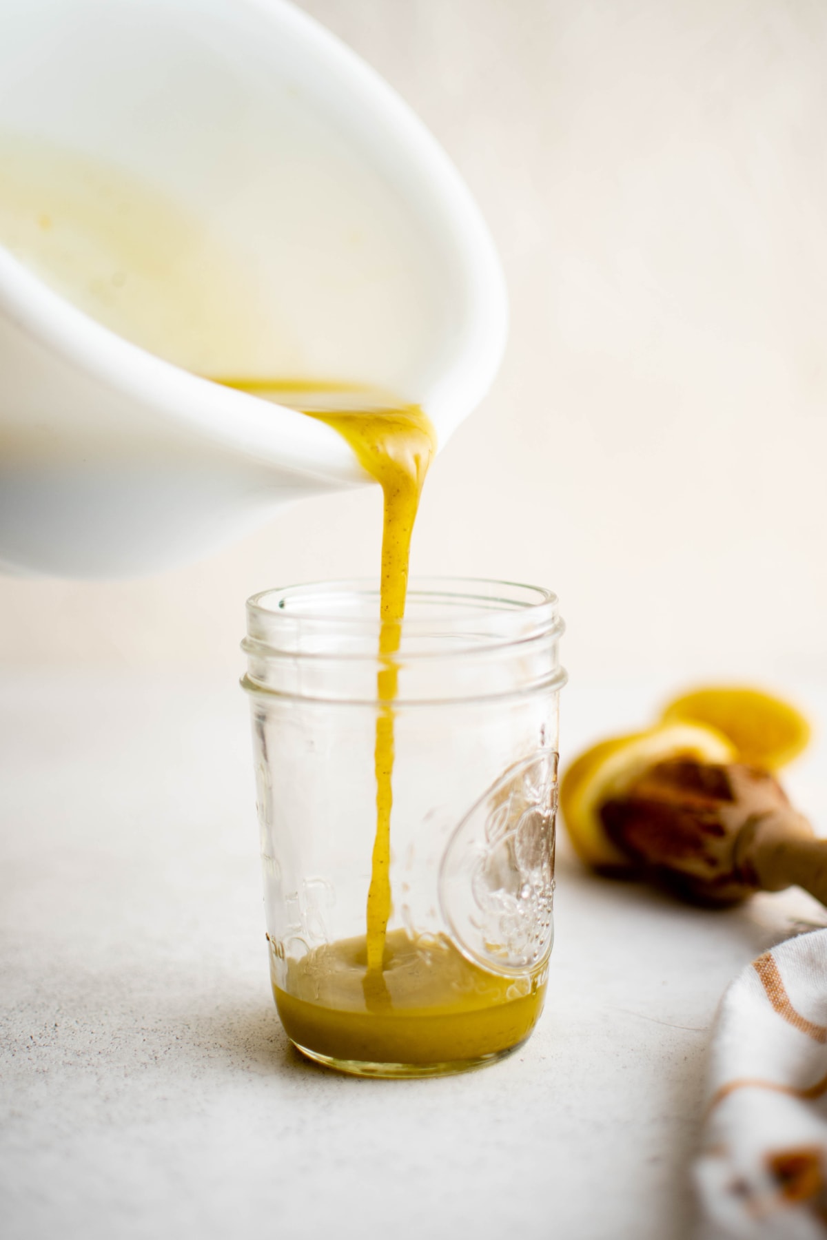 Pouring a vinaigrette from a white bowl into a glass jar.