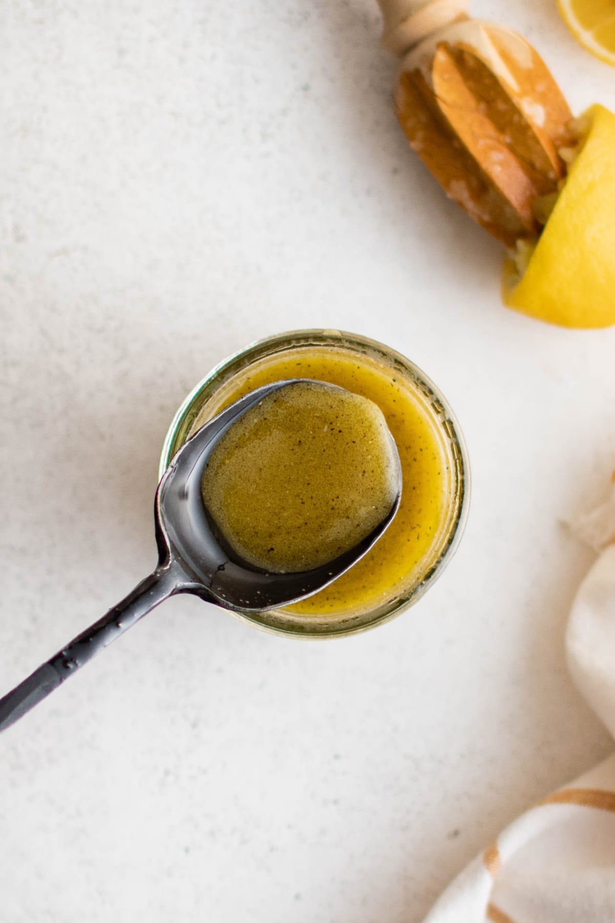 Glass jar with lemon vinaigrette and a spoon.