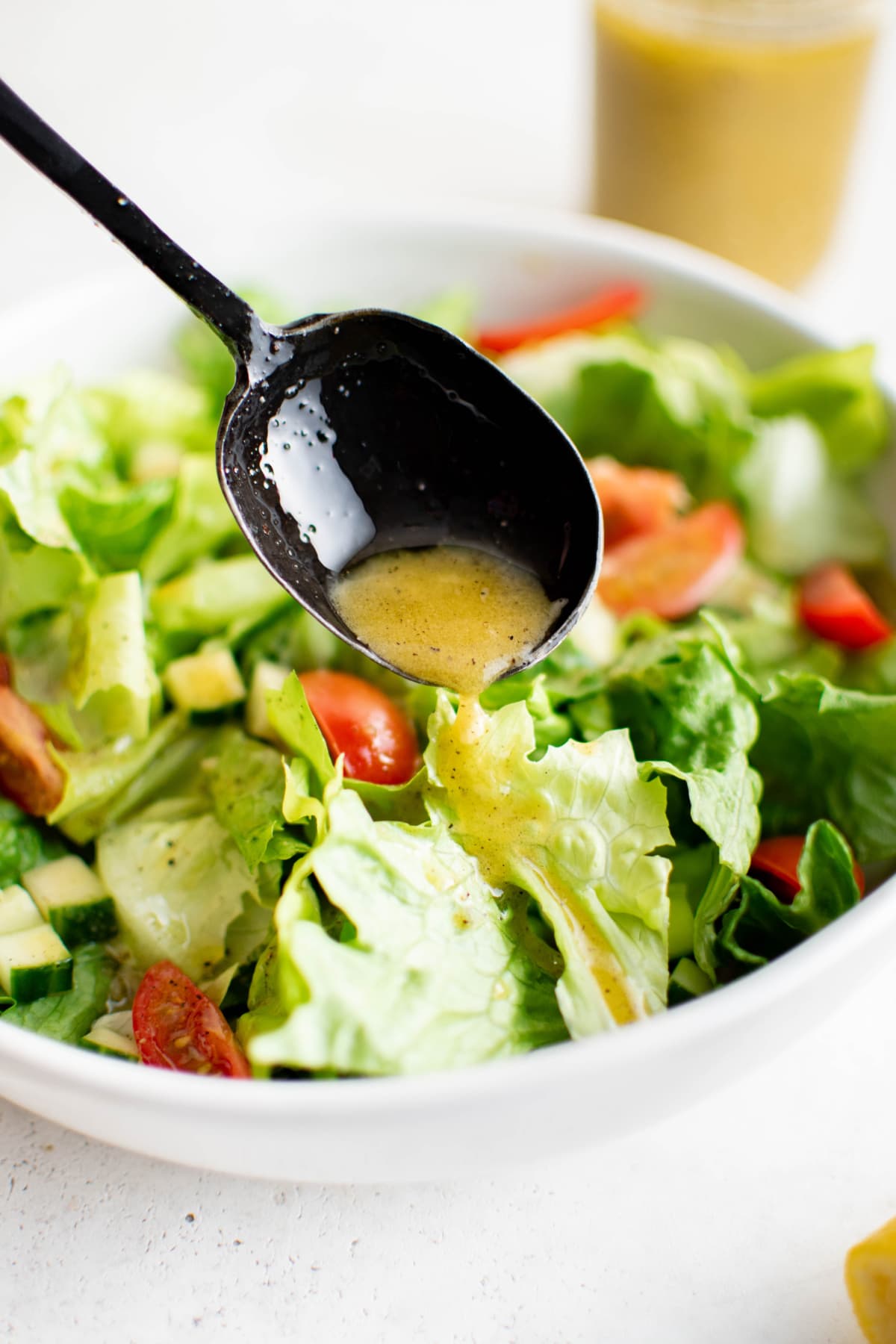Lettuce and tomatoes in a white bowl with a spoon drizzling lemon vinaigrette.