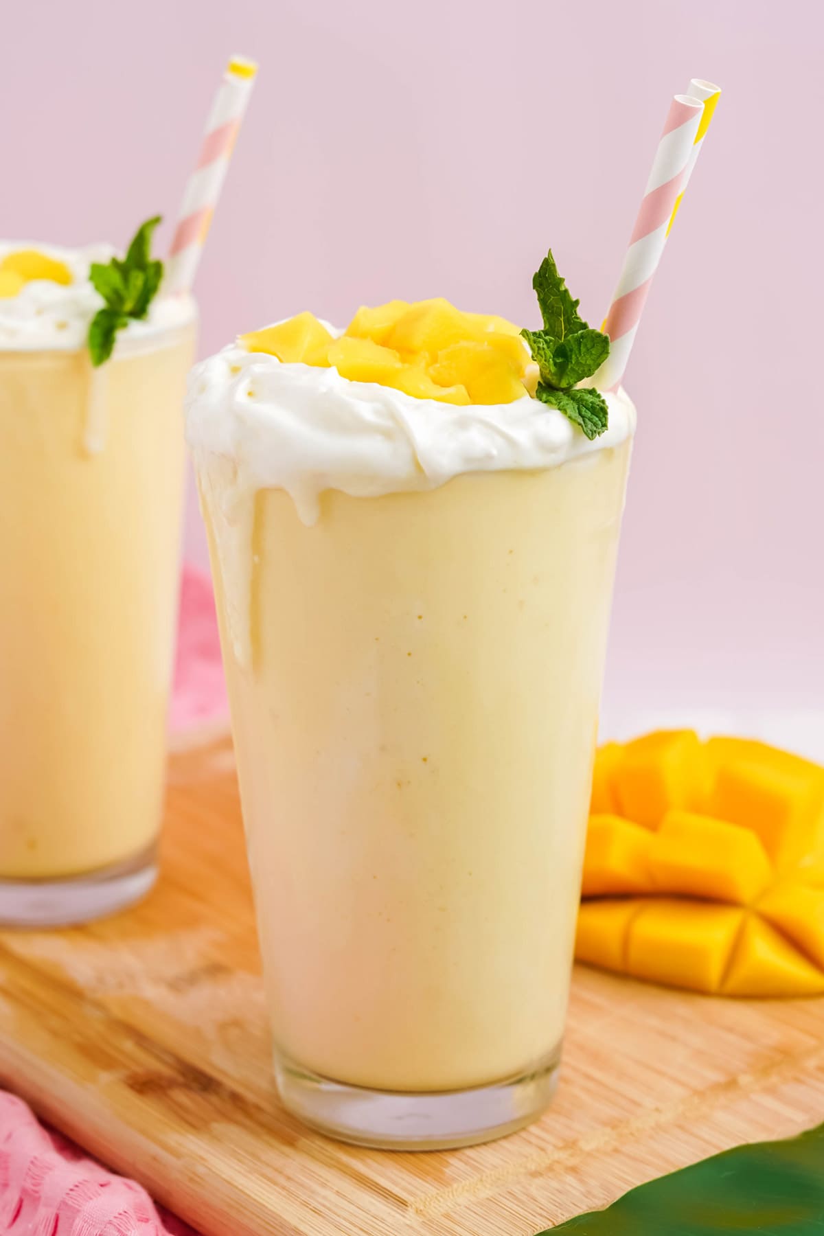 Mango milkshakes, chut mango, cutting board and a pink napkin.