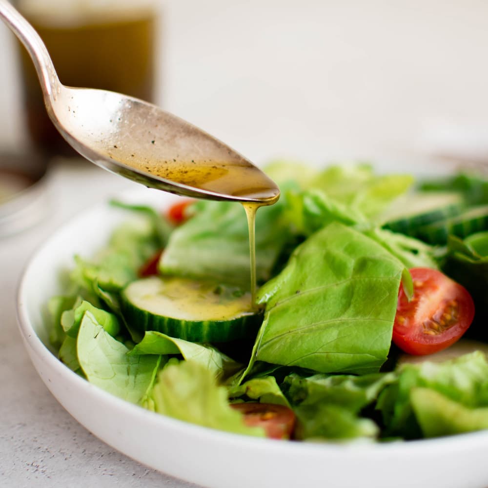 Oil and vinegar dressing on a spoon, drizzled over a salad.