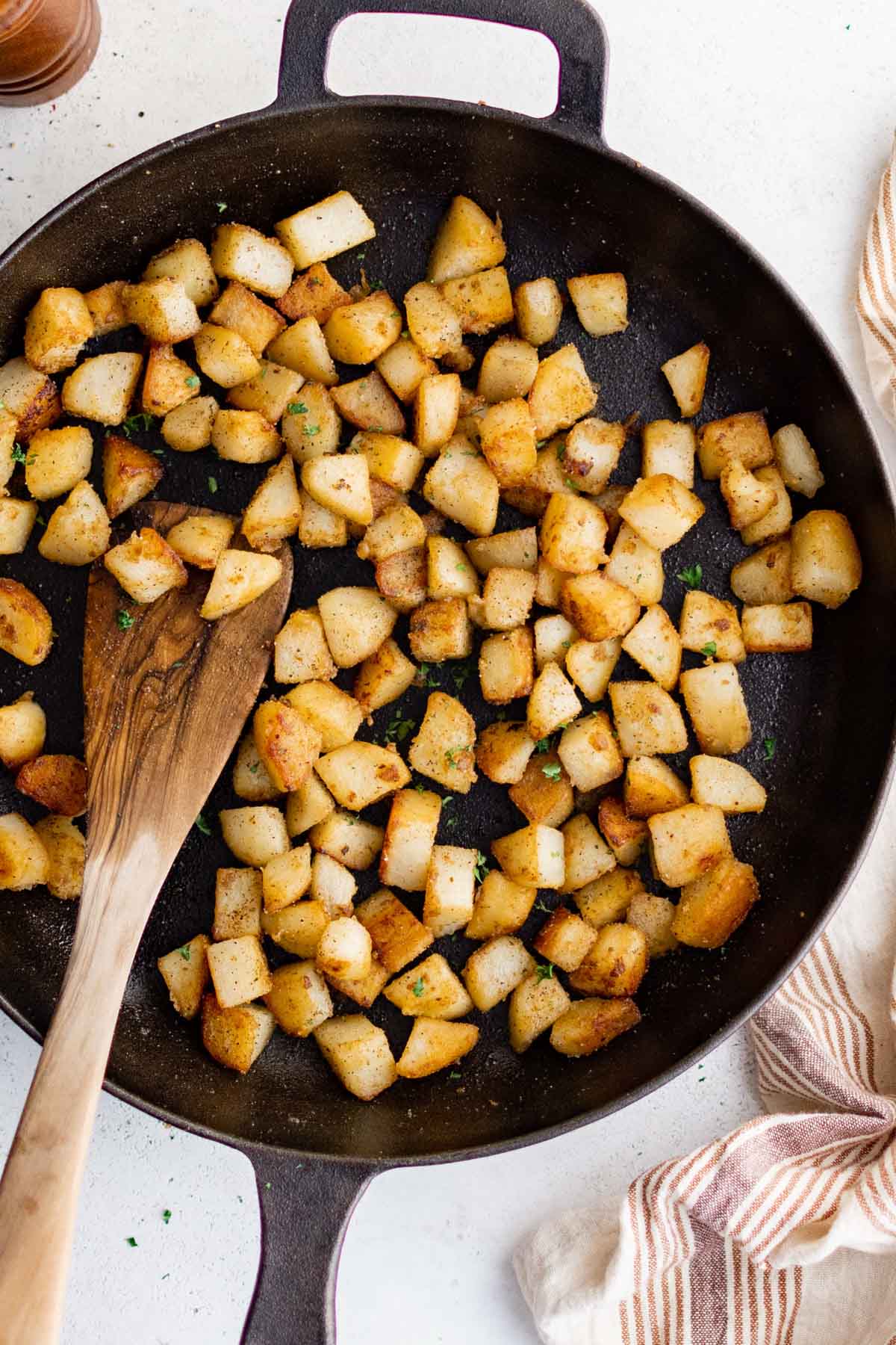Cast iron skillet with diced crispy potatoes and a wooden spoon.