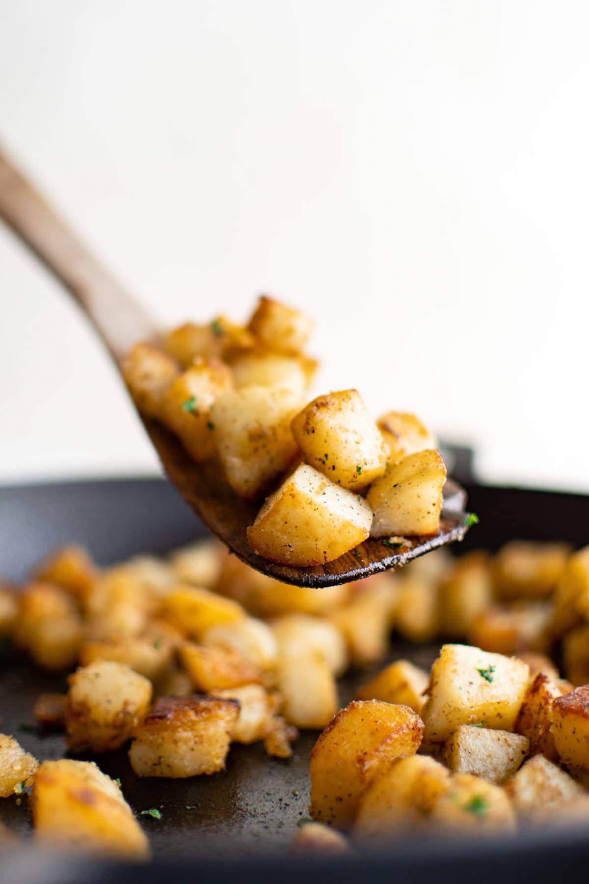 Wooden spoon with a serving of skillet potatoes over a cast iron skillet.