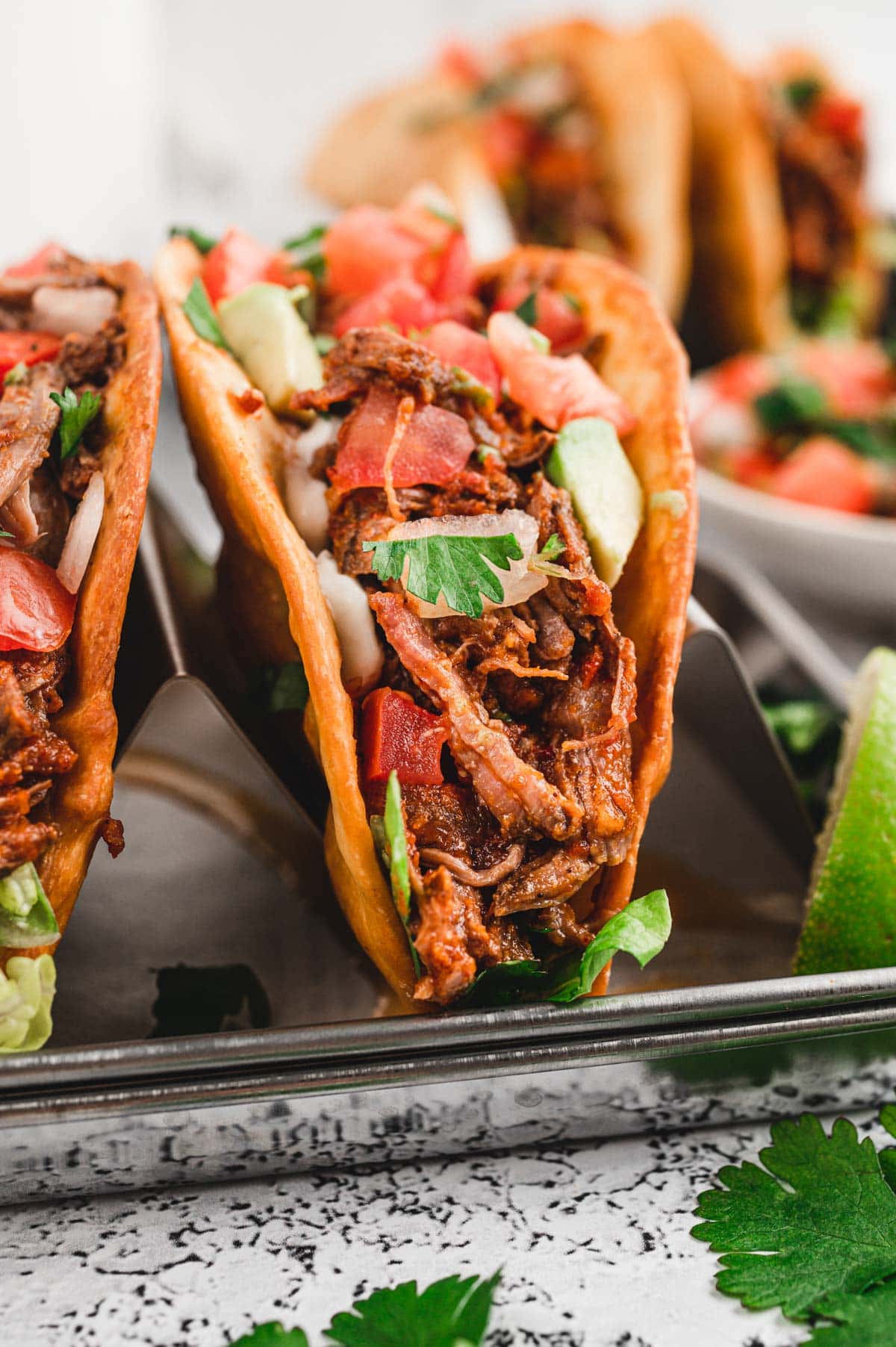 Shredded beef taco standing up, topped with tomatoes.