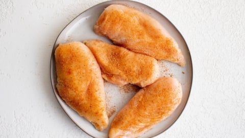 Raw chicken breasts with seasoning on a plate.