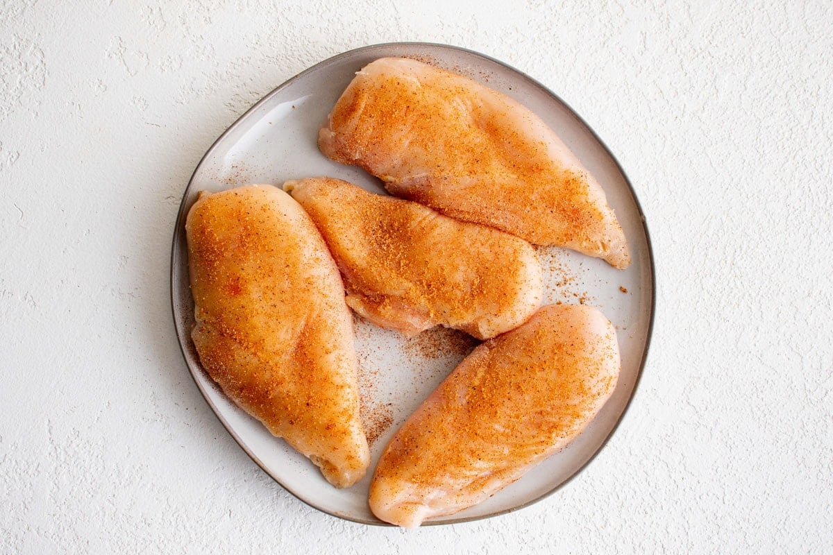 Raw chicken breasts with seasoning on a plate.