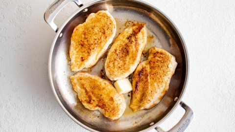 Seared chicken breasts in a skillet with a pat of butter.