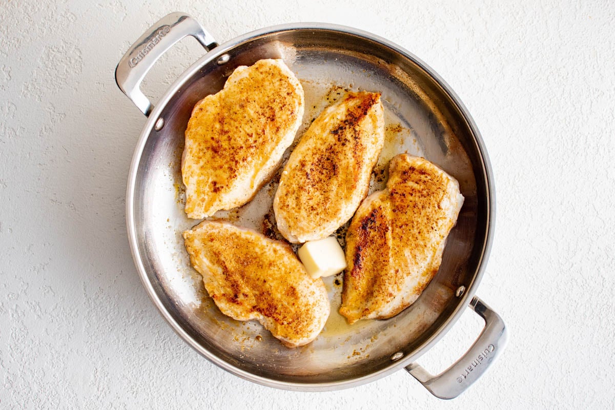 Seared chicken breasts in a skillet with a pat of butter.