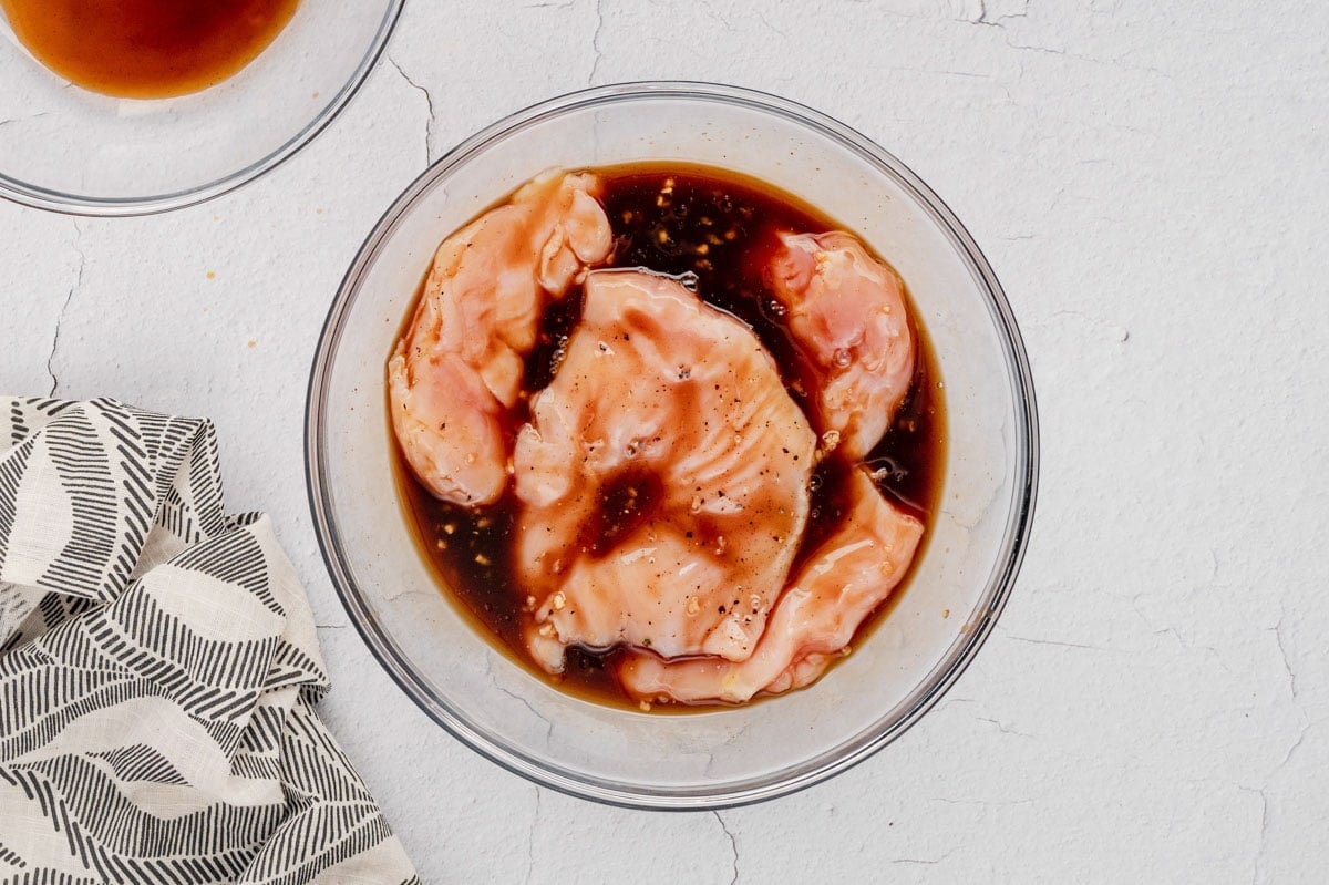raw chicken breasts in a marinade in a large bowl.