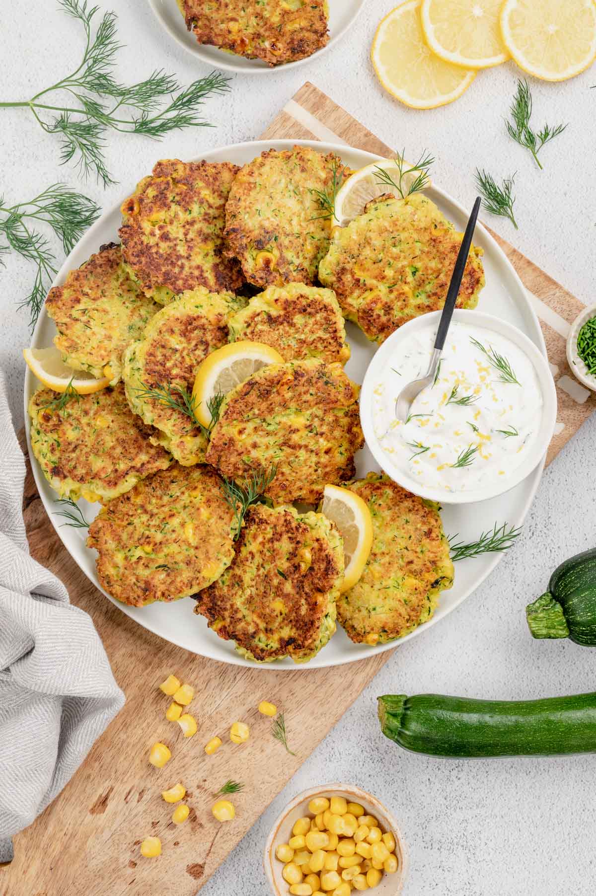 Fritters in a stack on a plate with a dish of creamy white sauce and a spoon.