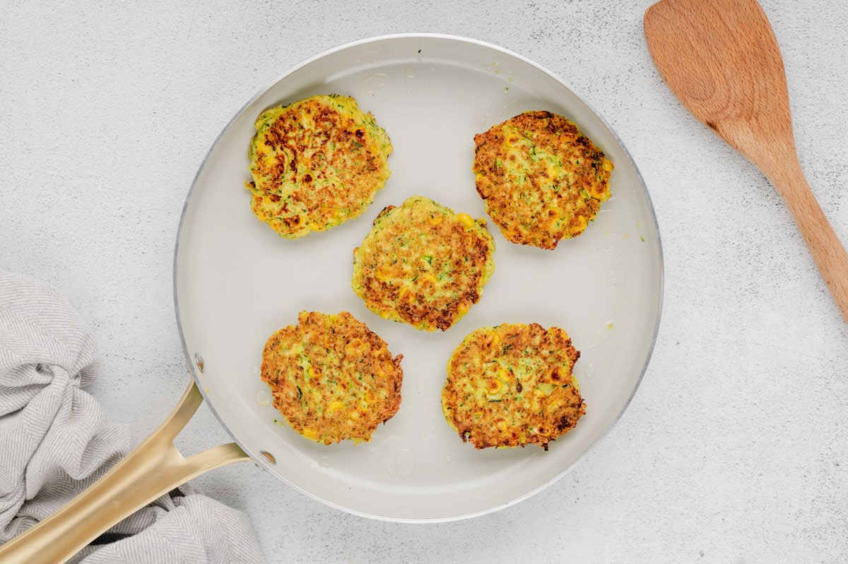 Fried zucchini fritters in a skillet.