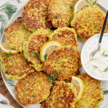 Fritters in a stack on a plate with a dish of creamy white sauce and a spoon.
