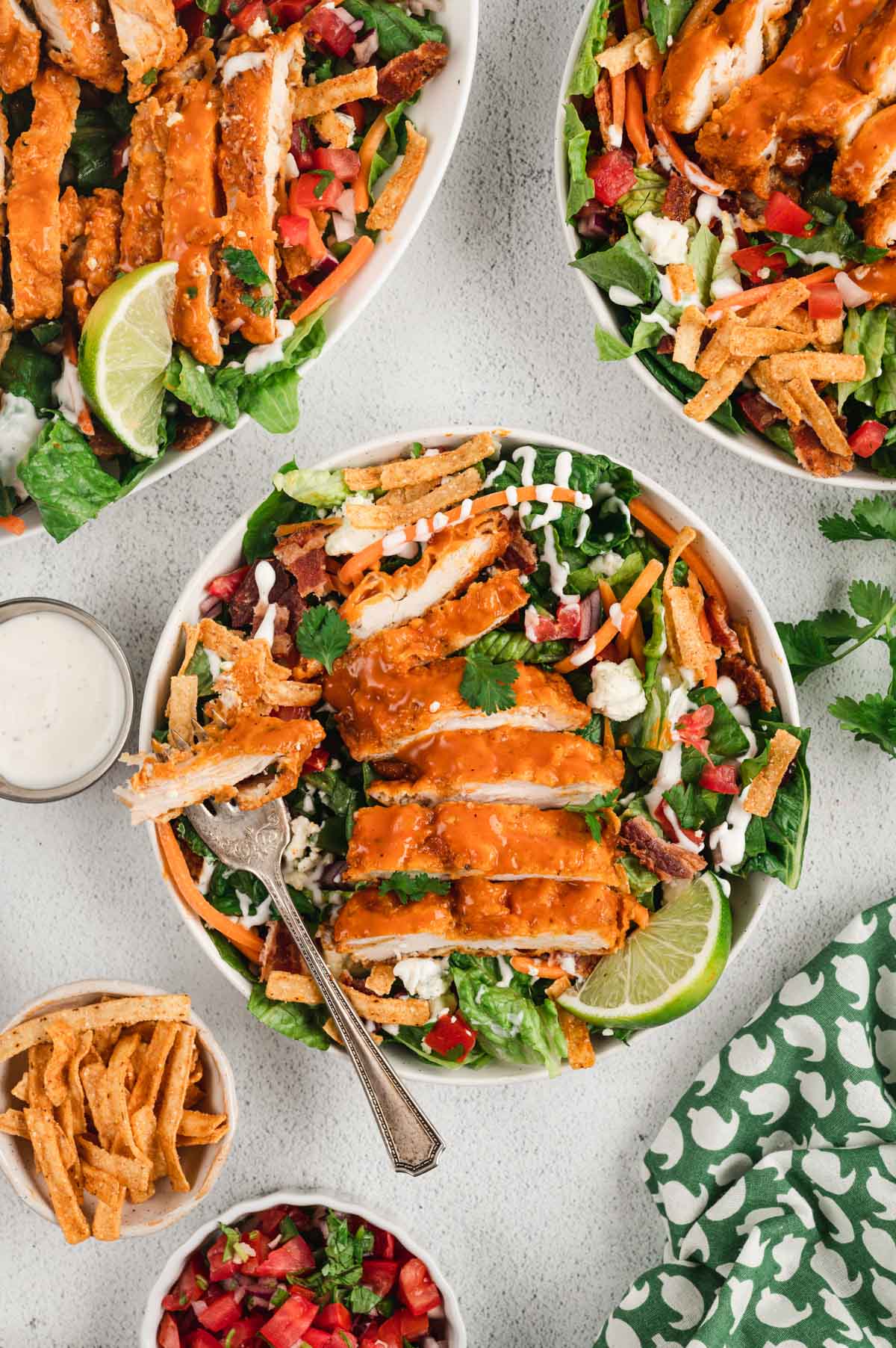 bowls of buffalo chicken with salad and small bowls of tortilla strips and pico de gallo.