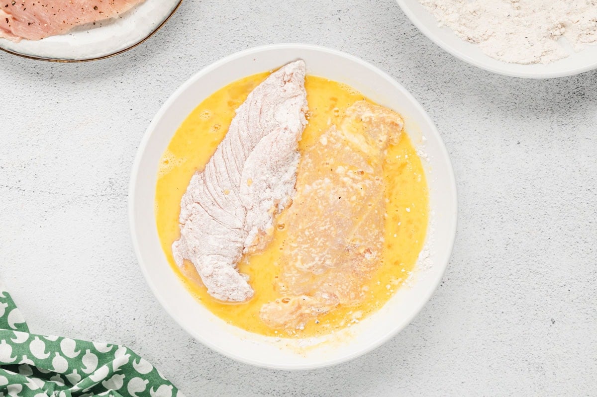 Flour coated chicken breast in an egg wash.
