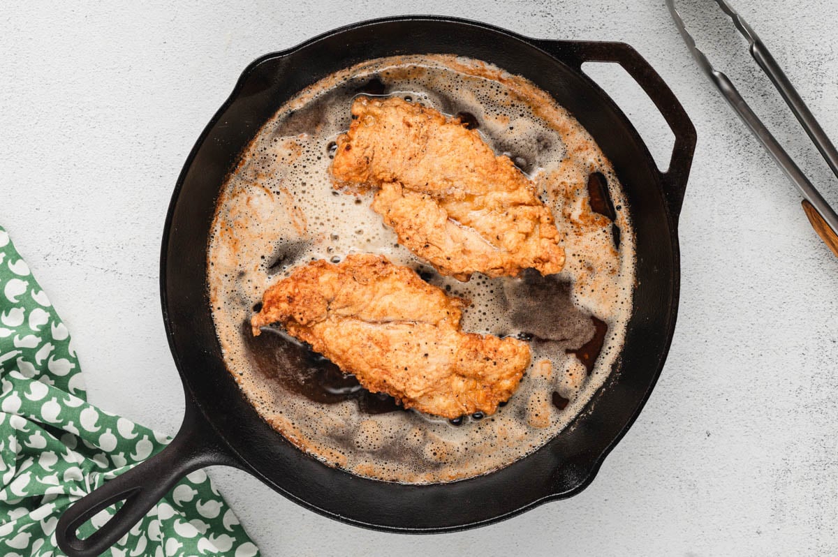 Breaded chicken breast frying in a skillet.