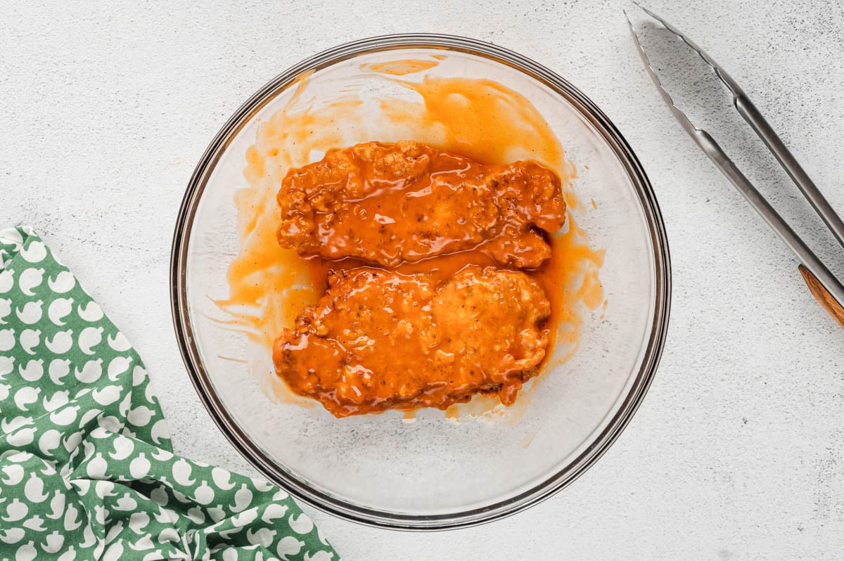 Crispy chicken breasts in a large bowl with buffalo sauce.