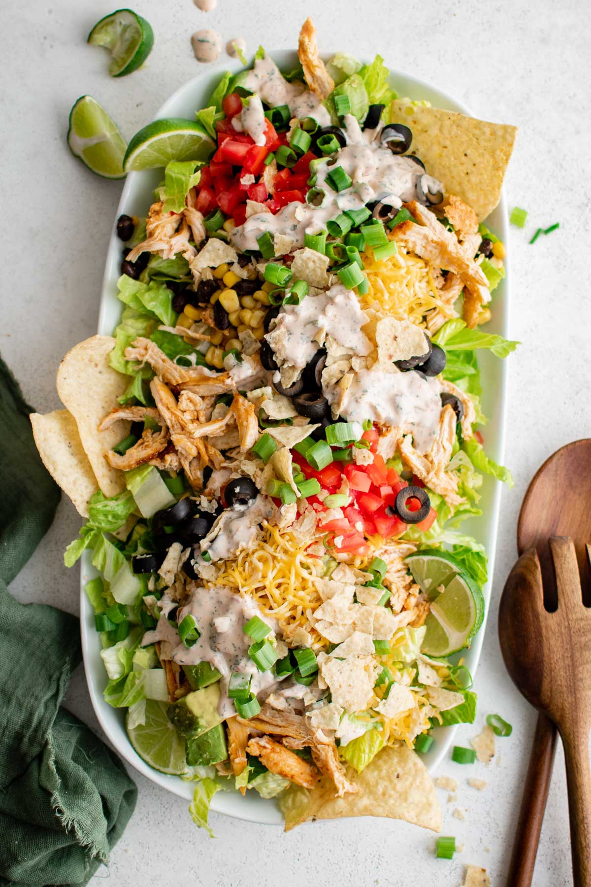 Layers of shredded romaine lettuce, tomatoes, chicken and cheese on a large white platter.
