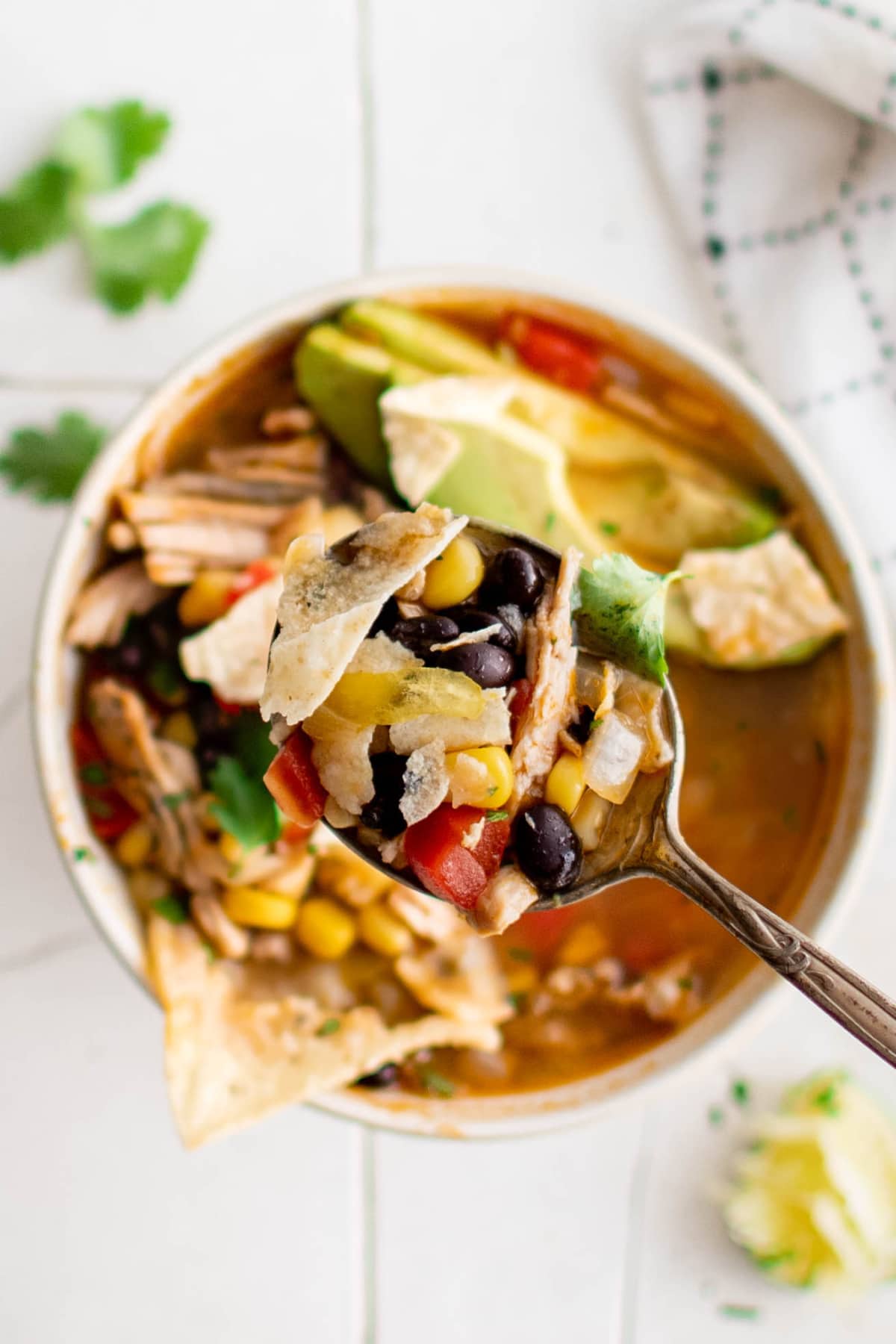 Bowl of chicken tortilla soup with a spoon lifting up a bit.