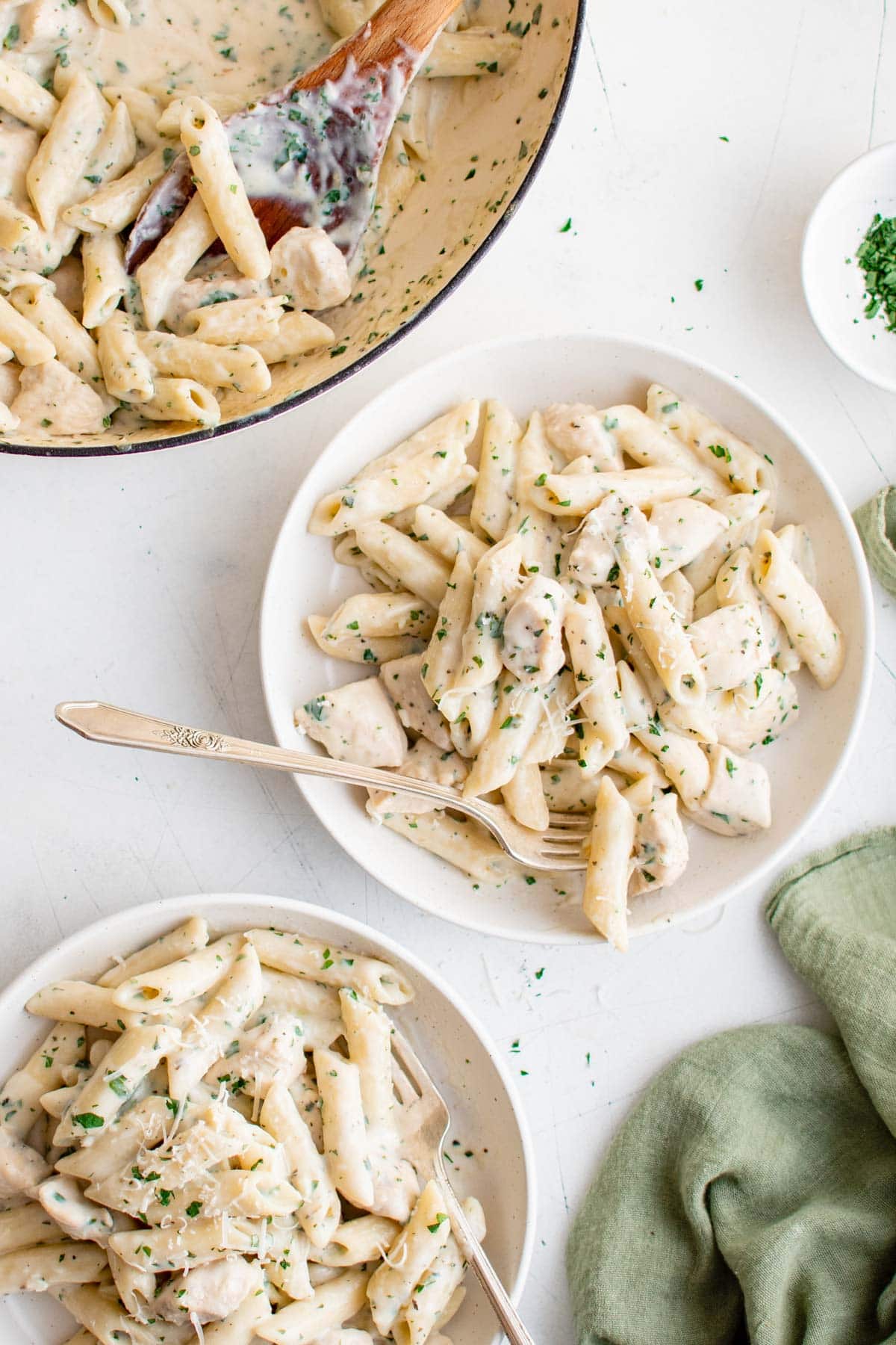 White plate with penne pasta in creamy sauce with chicken and a fork.