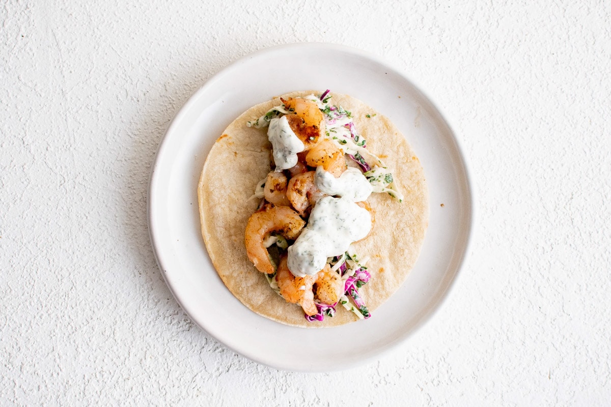 Plate with a tortilla filled with cabbage, shrimp and a creamy sauce.