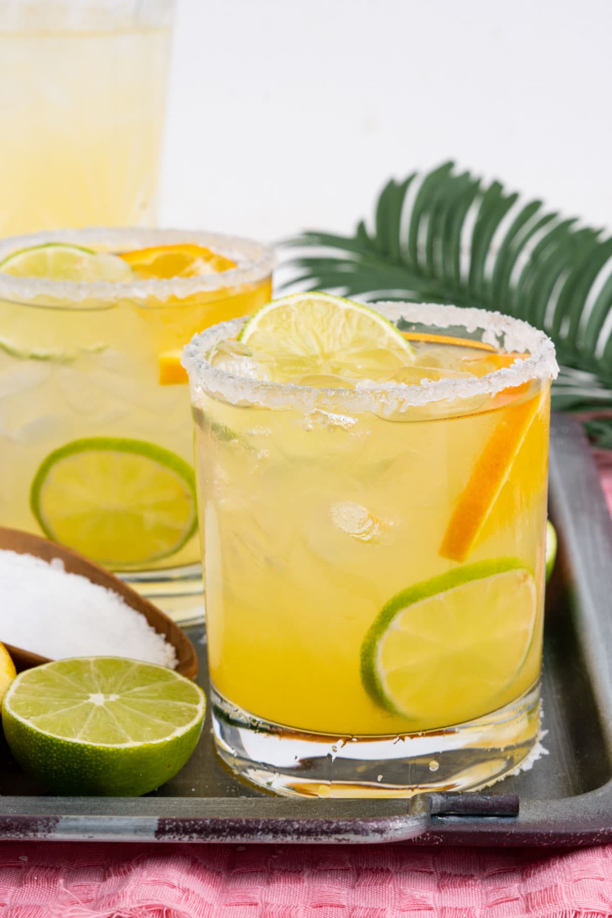 Margaritas in glasses with ice, limes and orange slices.