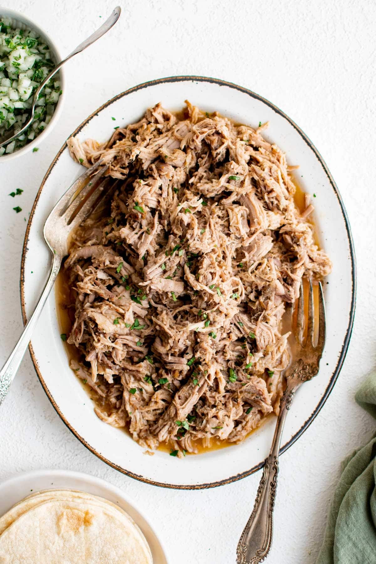 Shredded pork carnitas on a white platter with serving forks.