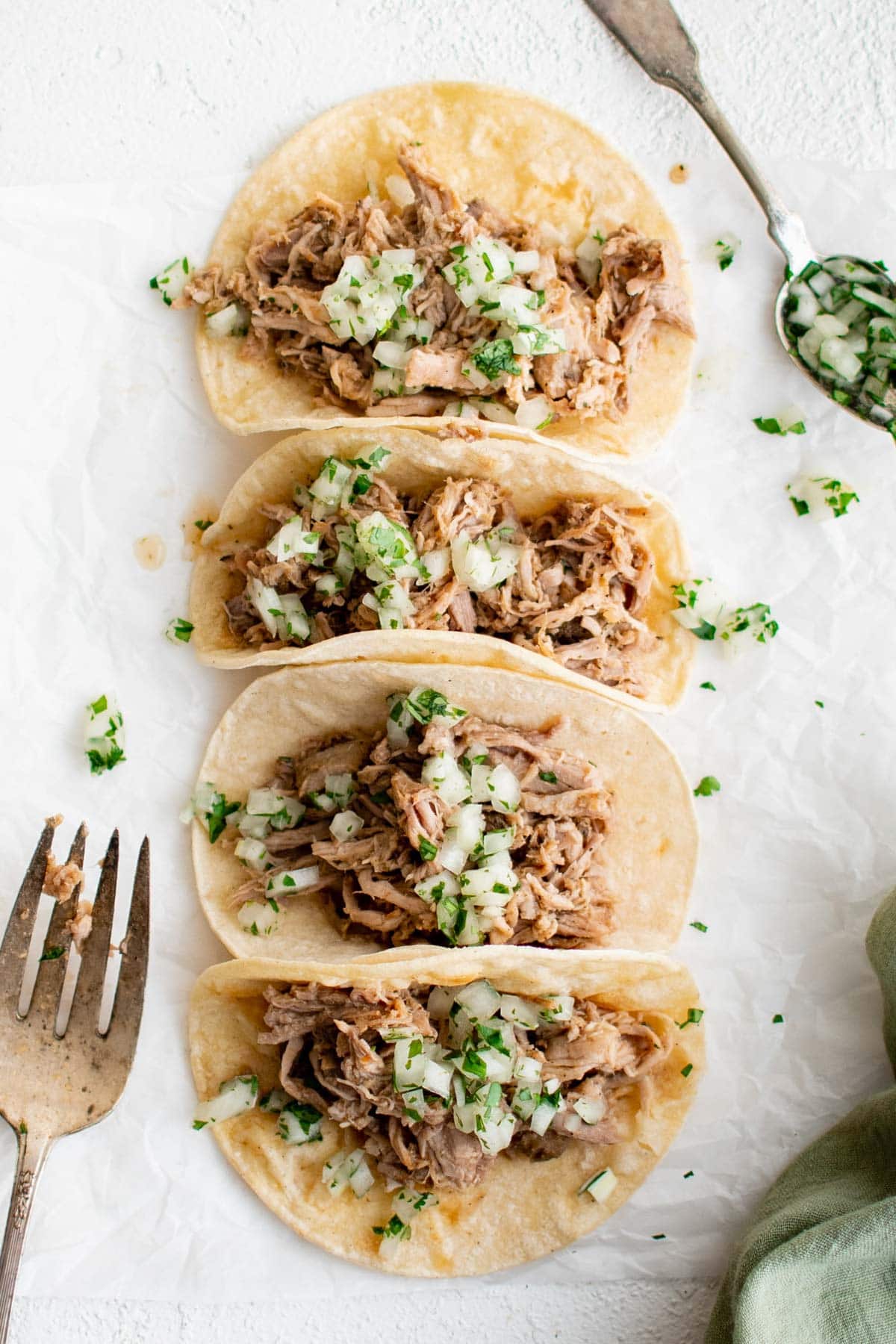 A row of carnitas tacos in corn tortillas.