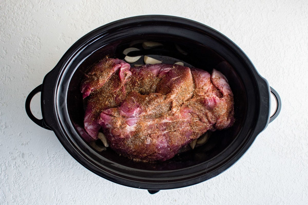 Pork butt roast in a slow cooker with spices.