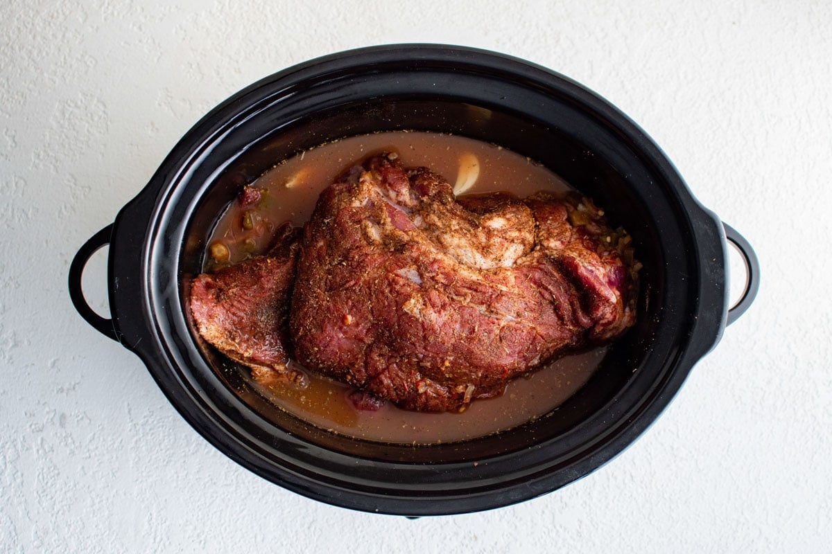 Pork butt with seasoning and juices in a slow cooker.