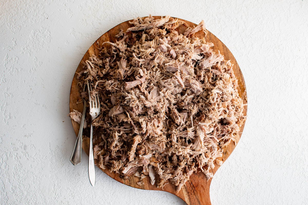 Shredded pork with two forks on a cutting board.