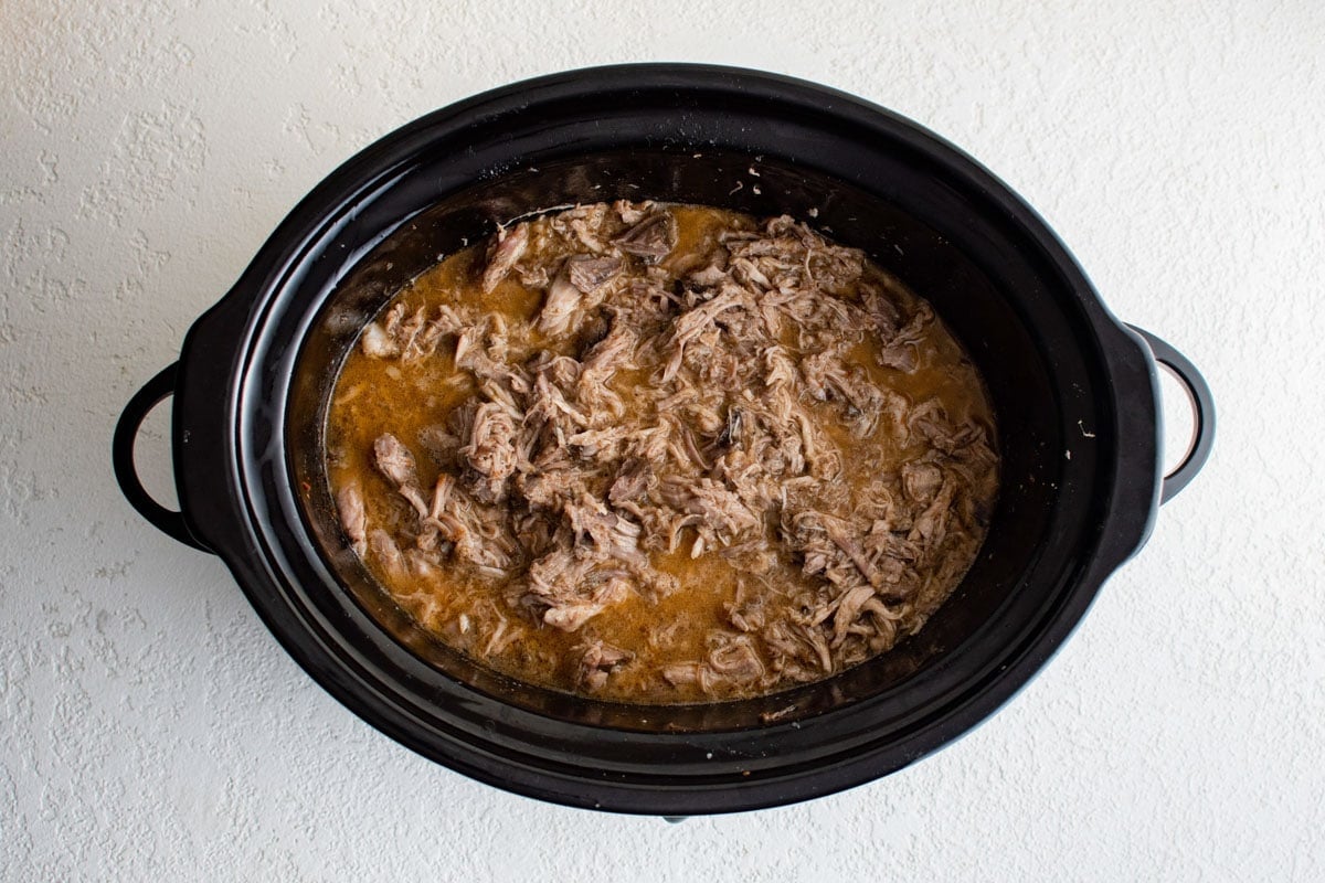 Shredded pork in liquid in a crock pot.