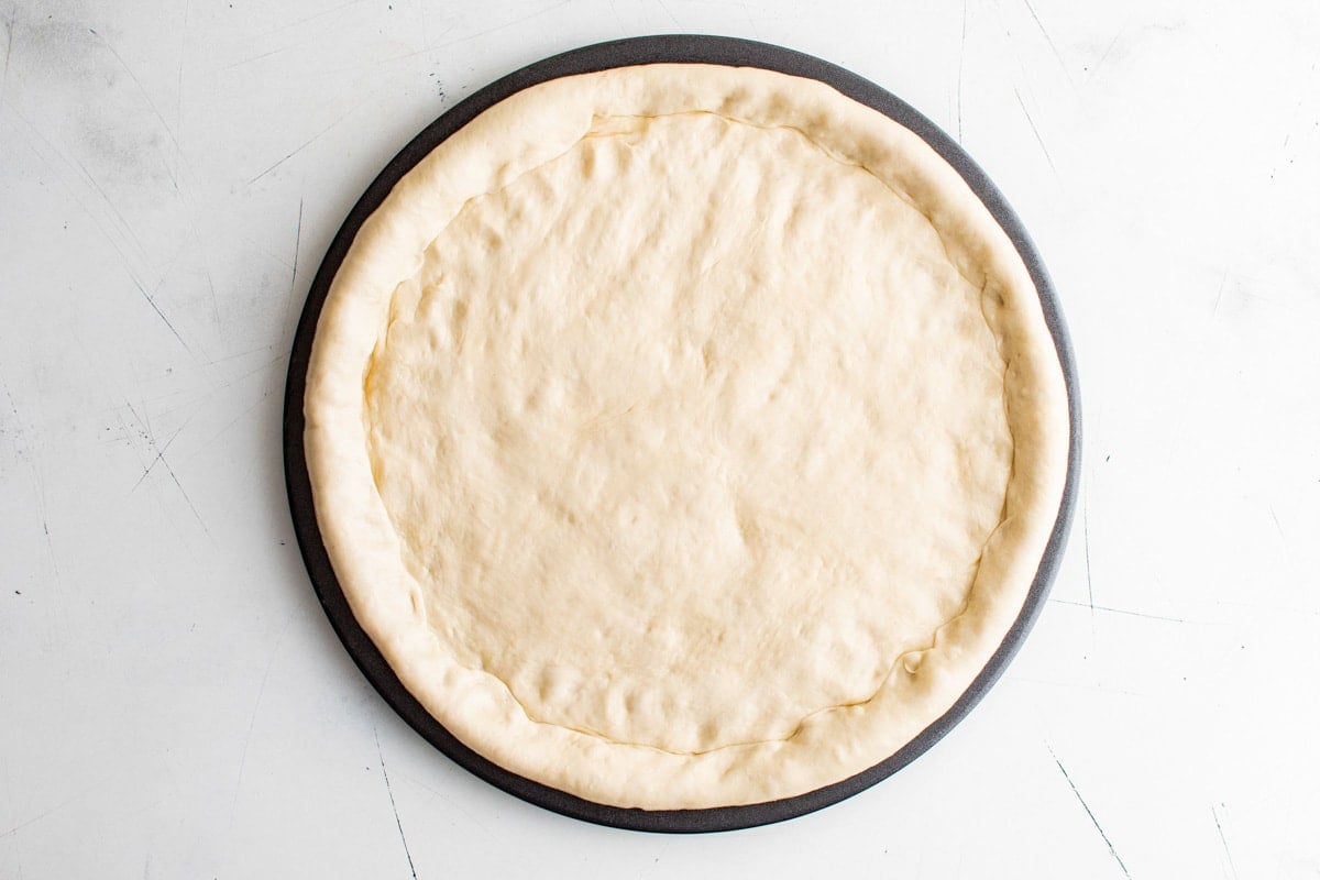 Pizza dough pressed into a pizza pan.