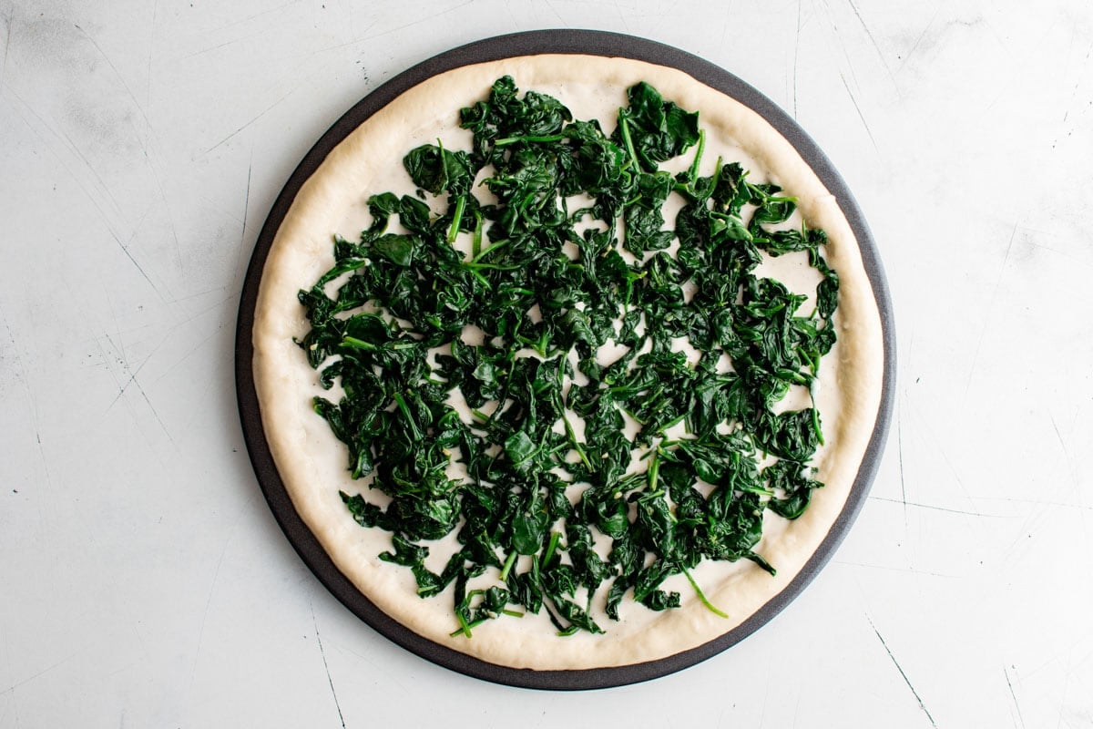 Pizza dough with alfredo sauce and wilted spinach.