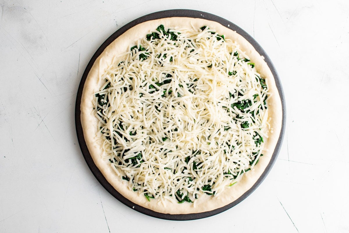 Pizza dough in a pan topped with spinach and shredded cheese.