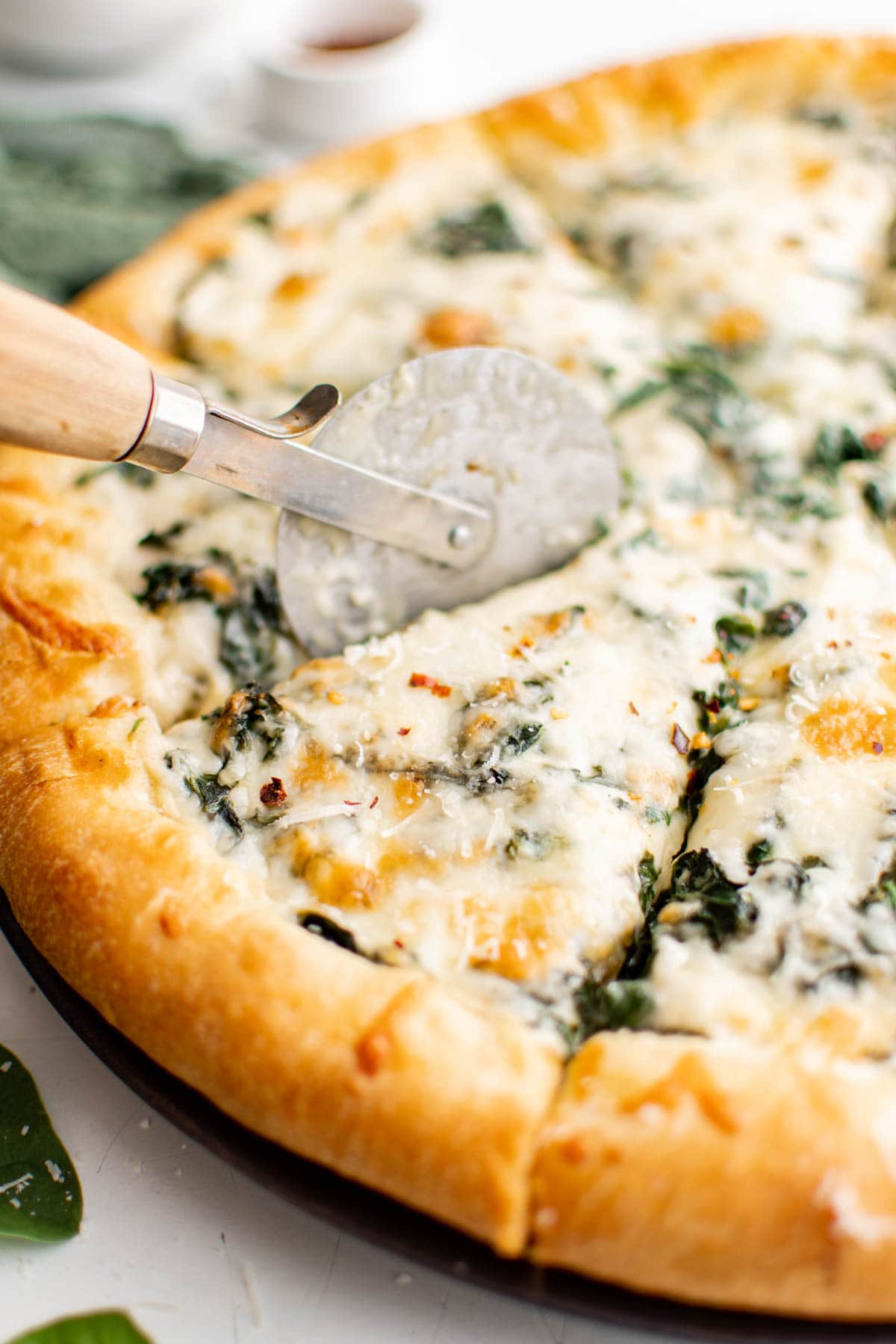 Spinach alfredo pizza sliced with a pizza cutter.