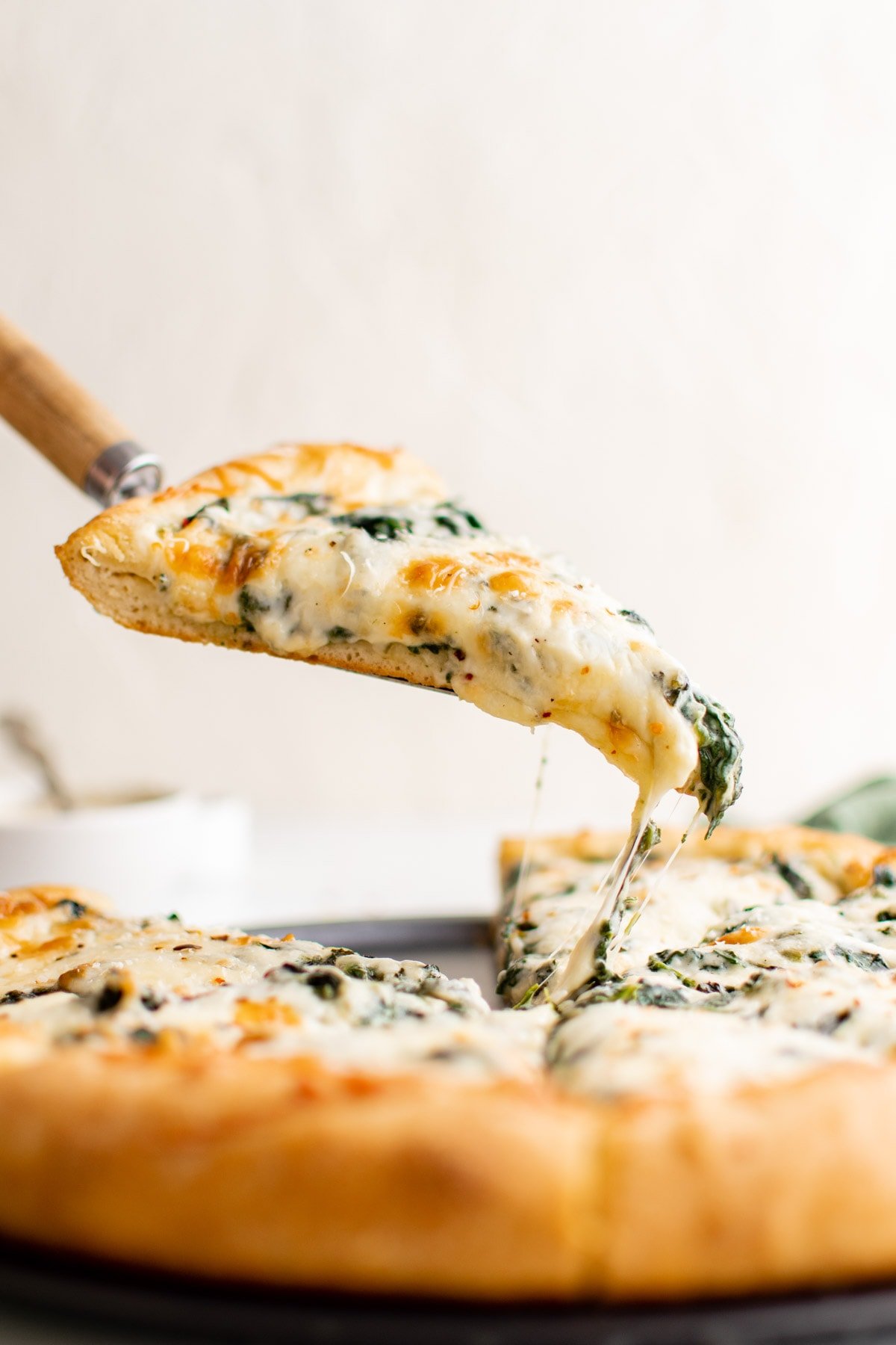 Spinach Alfredo Pizza, with a spatula lifting one slice.