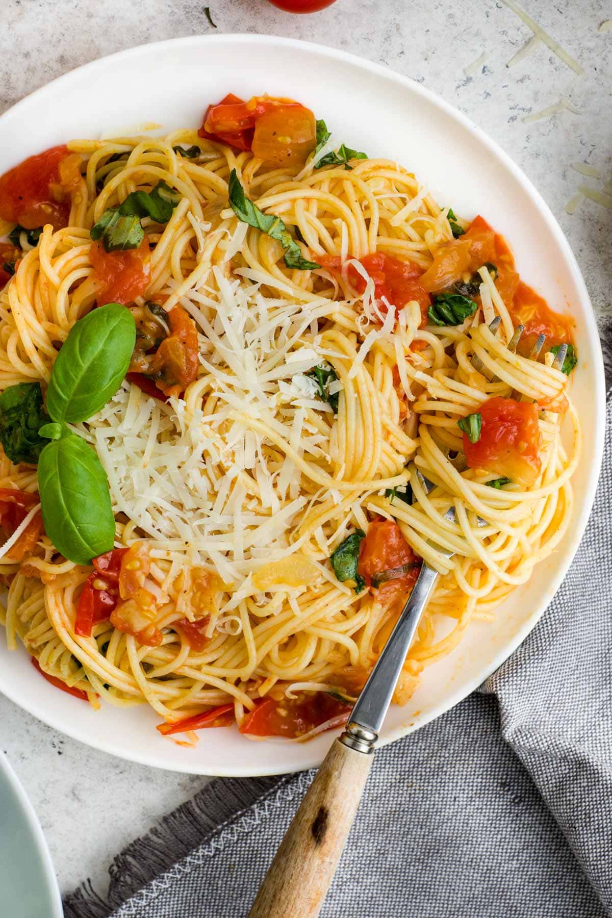 White shallow dish with angel hair pasta, tomatoes and basil.