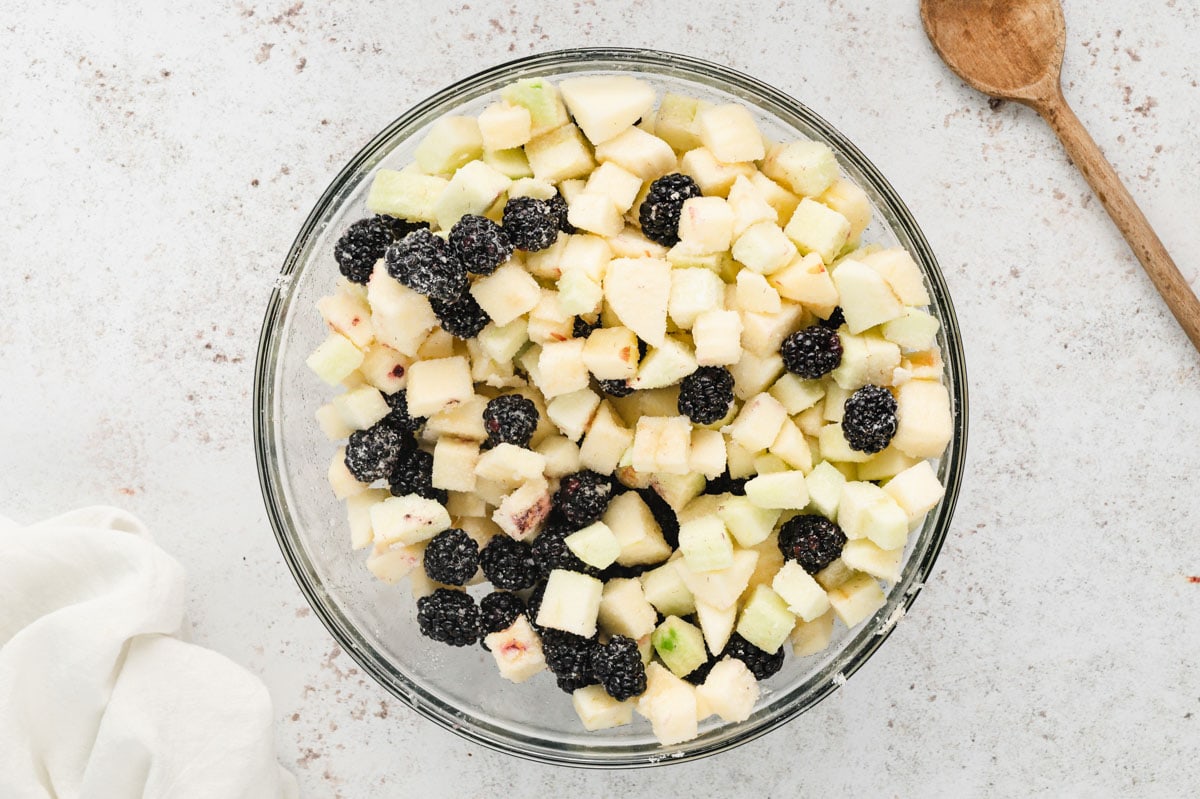 Diced apples and blackberries in a clear glass mixing bowl.