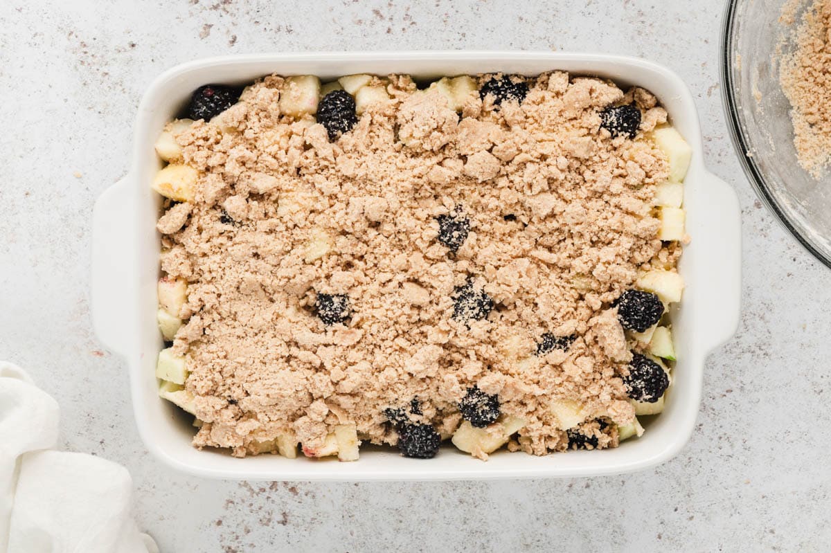 Diced apples and blackberries in a white dish with crumbled dough topping.