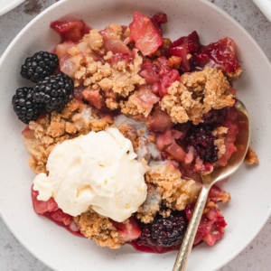 Apple blackberry crumble in a bowl with vanilla ice cream.