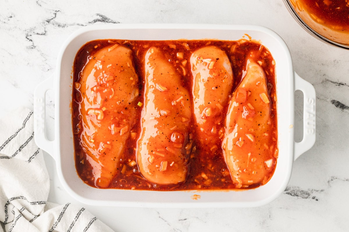 4 chicken breasts in a baking dish with sauce.