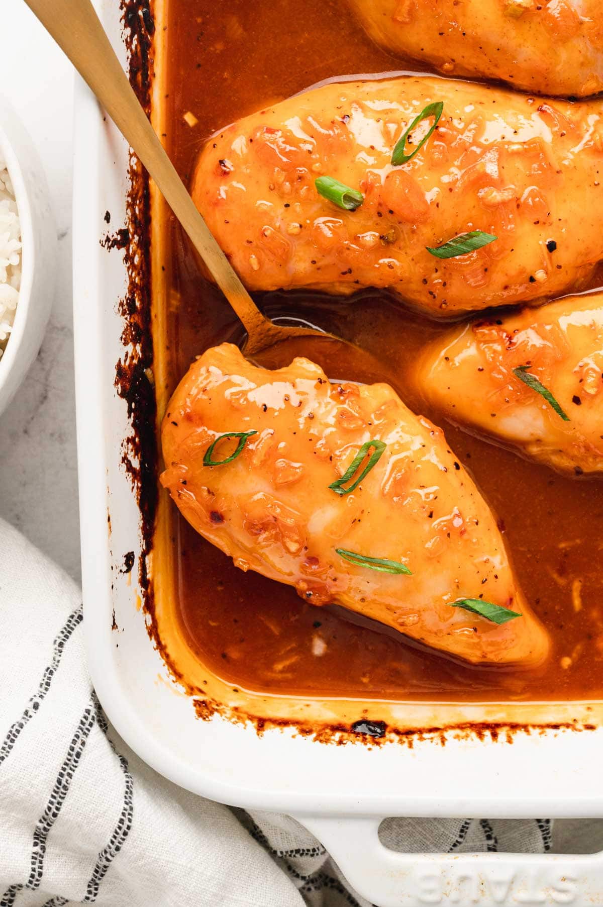 Apricot chicken breasts in a white baking dish, a gold serving spoon.