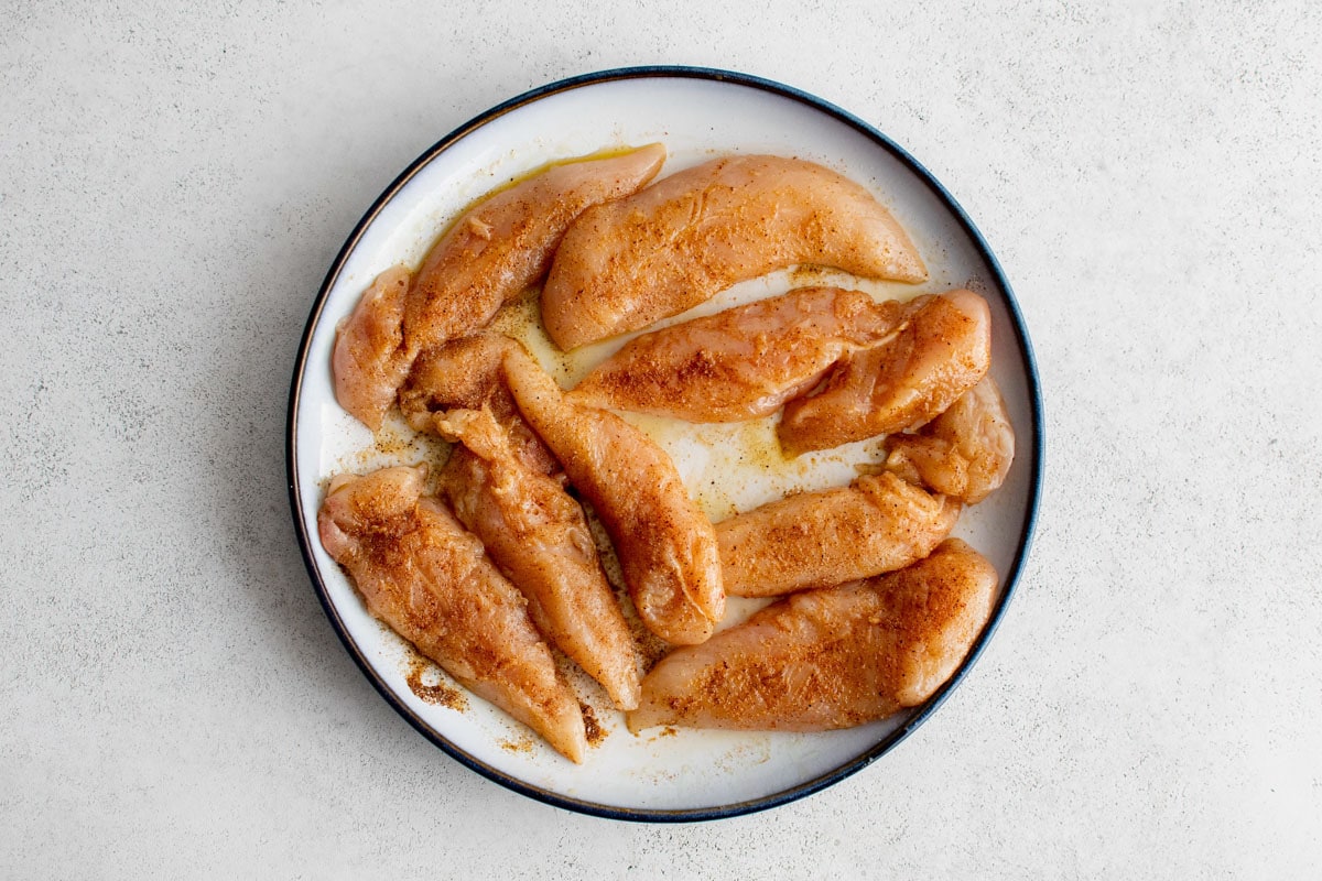 Season raw chicken tenders on a plate.