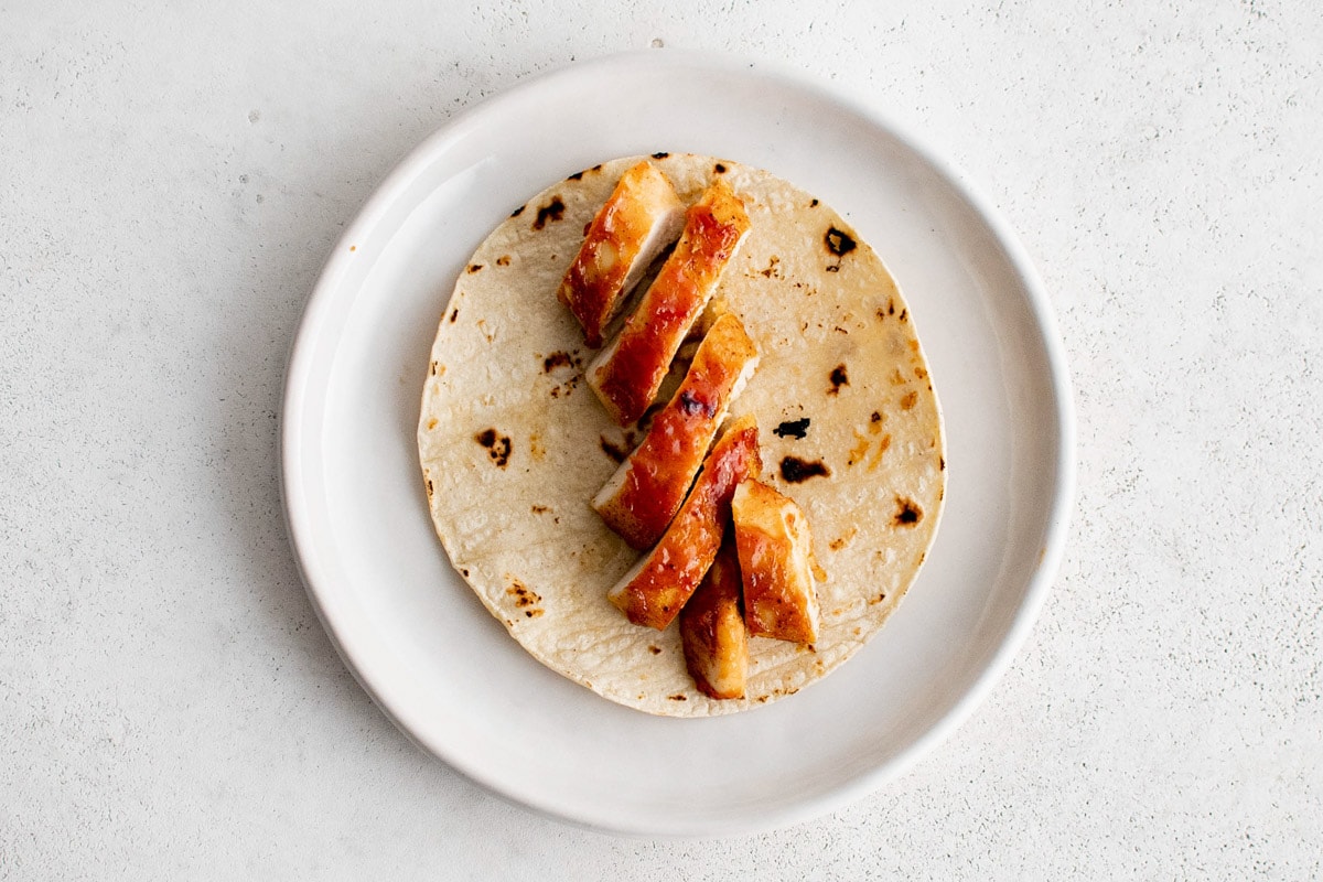 Sliced chicken on a tortilla on a plate.