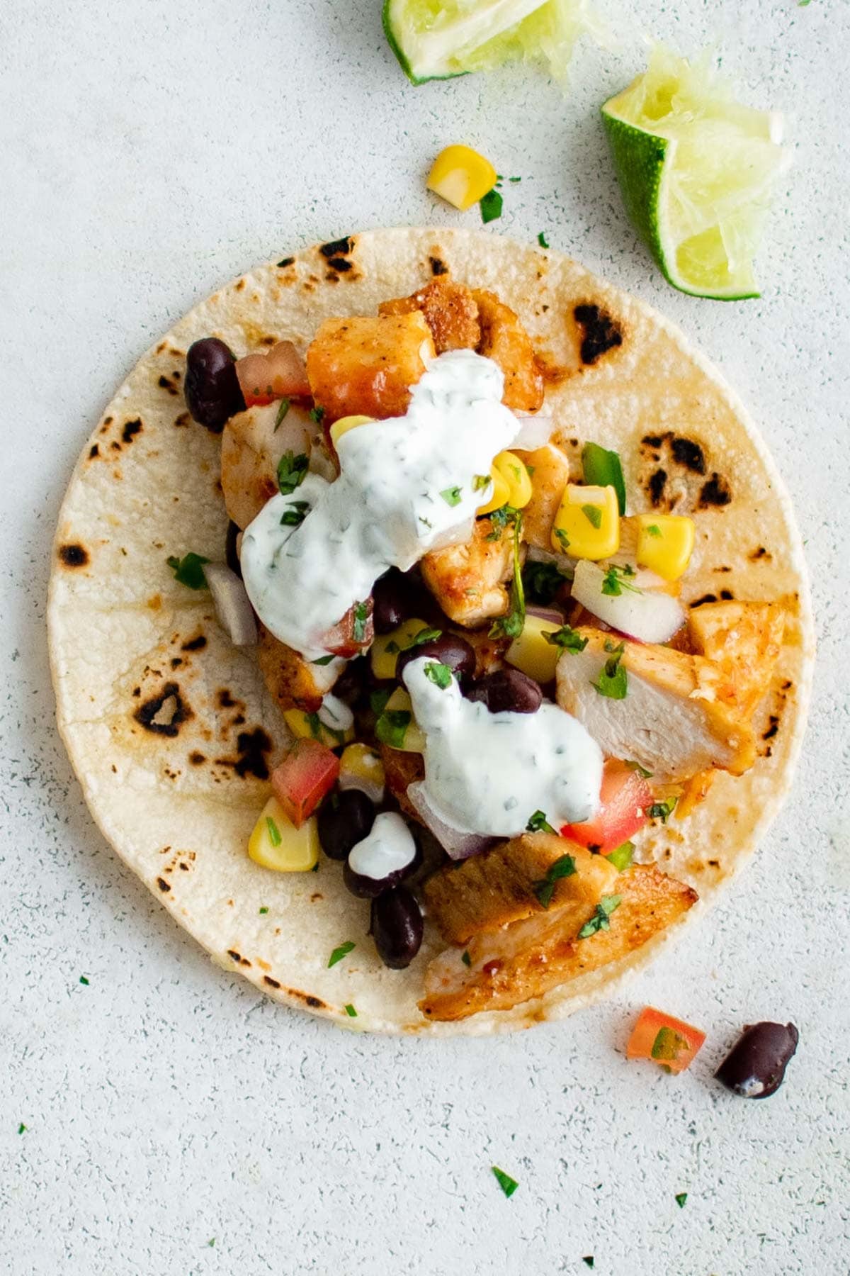 A charred corn tortilla with bbq chicken, black bean salsa and lime cilantro crema on top.