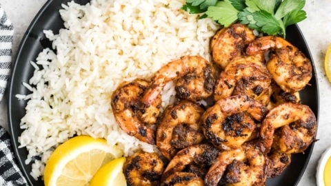 Blackened shrimp, rice, lemon slices and parsley on a black plate.