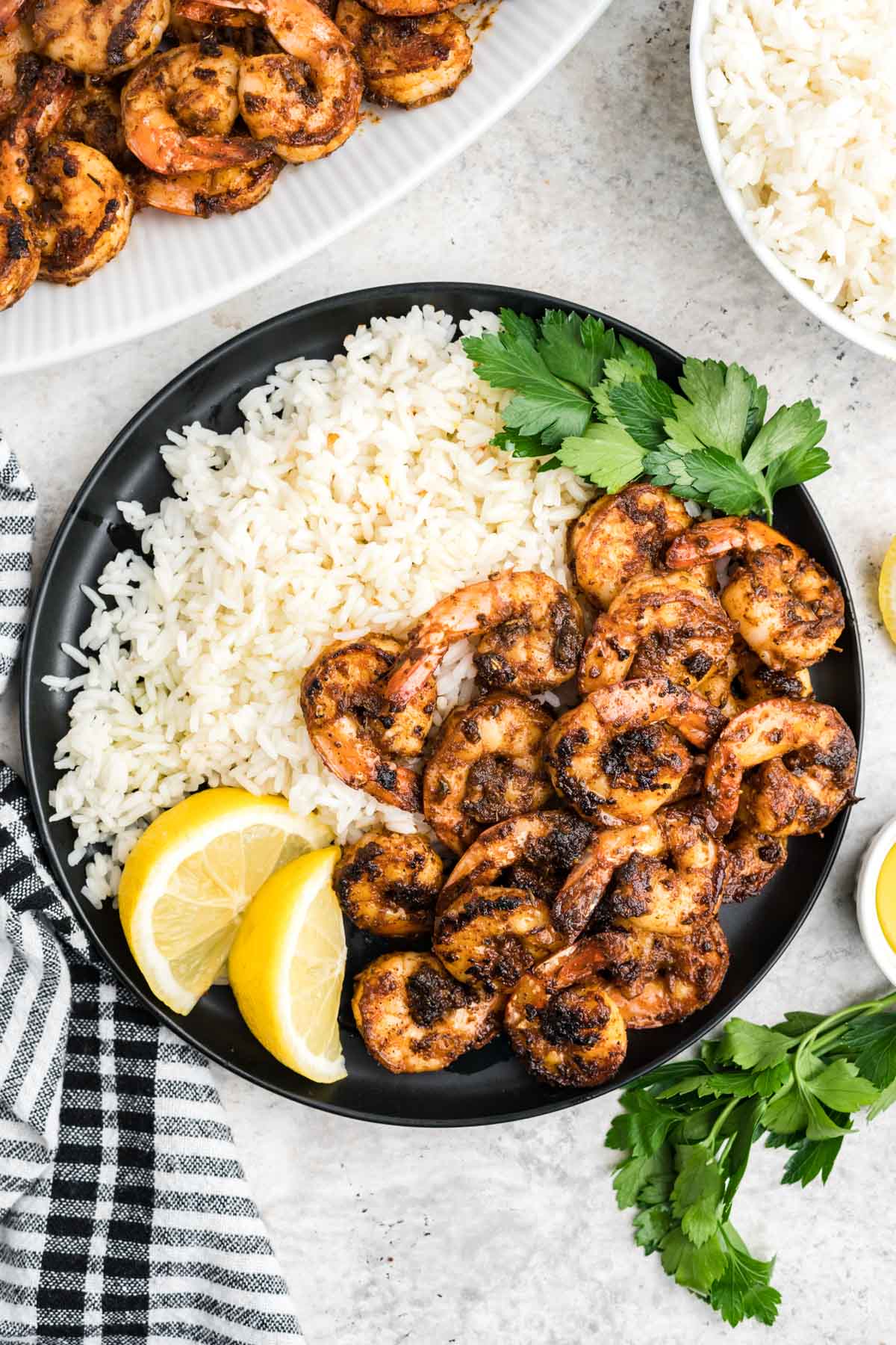 Blackened shrimp, rice, lemon slices and parsley on a black plate.