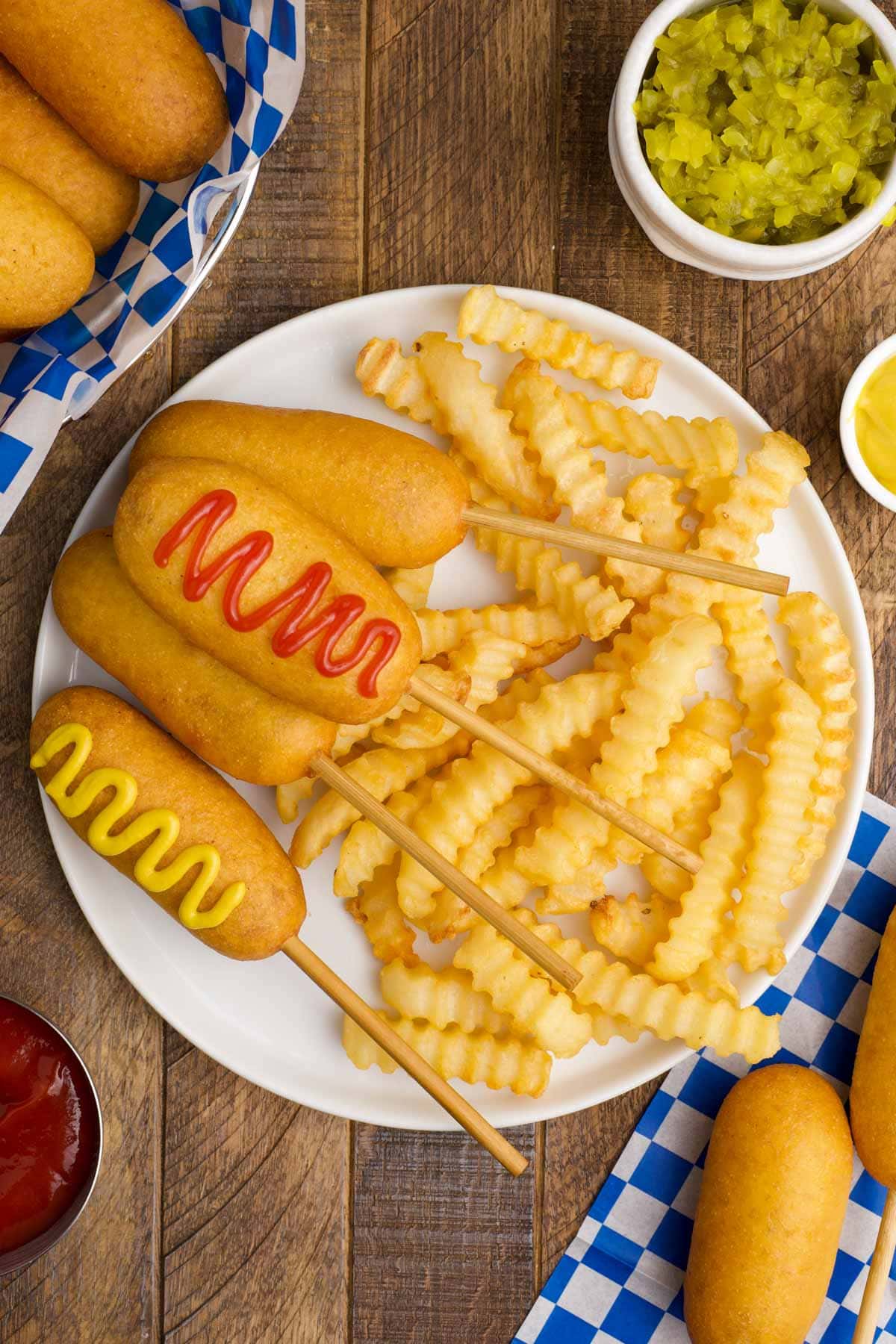 Corn dogs with ketchup and mustard and french fries on a white plate.